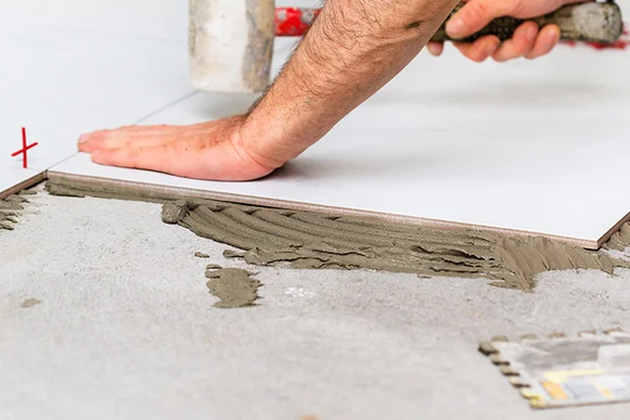 Person verlegt Fliese mit Gummihammer